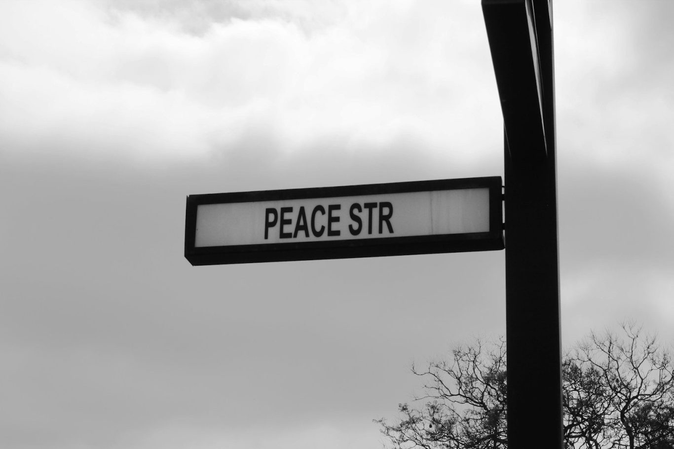Straßenschild mit der Aufschrift „PEACE STR“. Hintergrund in Schwarz-Weiß.