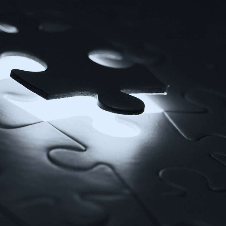 Ein Puzzlestück schwebt über einem dunklen Puzzle mit einer Lücke.