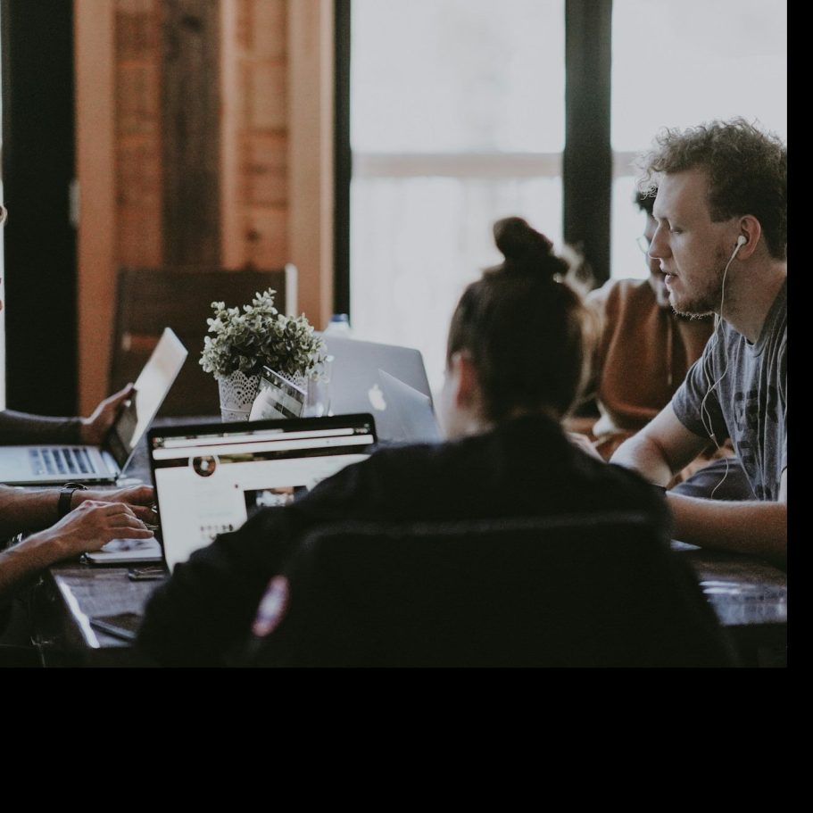 Gruppe von Menschen an einem Tisch, die an Laptops arbeiten und diskutieren.