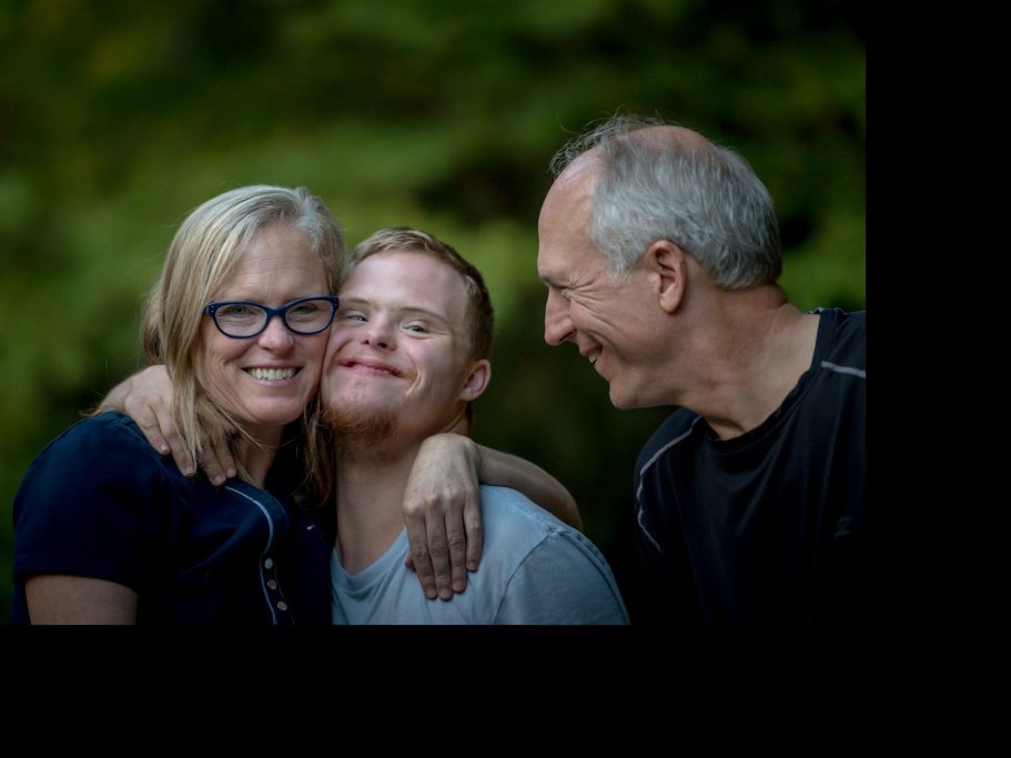 Eine glückliche Familie mit einem jungen Mann und seinen Eltern, die eng zusammenstehen.