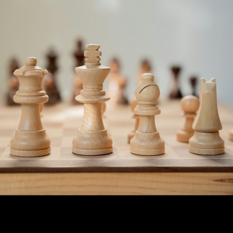 Vier Schachfiguren aus Holz, darunter ein König und eine Dame, auf einem Schachbrett.