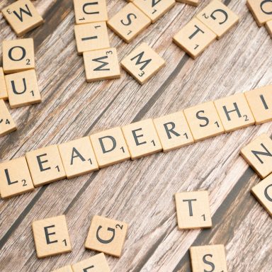 Buchstabenplättchen, die das Wort "LEADERSHIP" bilden, auf einer Holztischoberfläche.